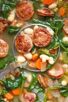 a spoon full of soup with sausage, beans and spinach in it's bowl