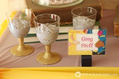 there are three glasses on the table with some stuff in them and a sign that says grey stuff