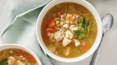 two bowls filled with soup on top of a white table next to silver spoons