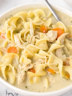 a white bowl filled with chicken noodle soup on top of a marble countertop