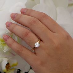 a woman's hand with a diamond ring on it and flowers in the background