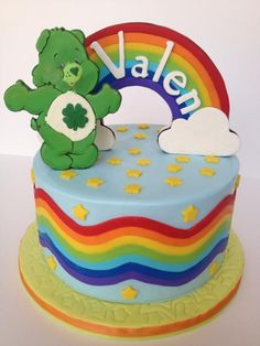 a rainbow cake with a teddy bear and name written on the top, in front of a white background