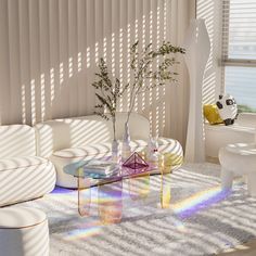 a living room filled with white furniture and lots of sunlight coming through the window blinds