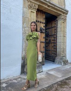 a woman standing in front of a door wearing a green dress with ruffles