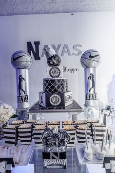 a table topped with cakes and desserts covered in black and white stripes next to a basketball themed wall