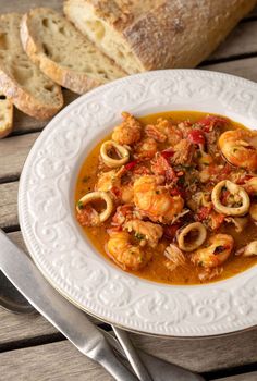 a white plate topped with pasta and shrimp next to some bread on a wooden table