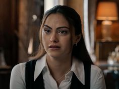 a woman in white shirt and black suspenders looking at the camera with serious look on her face