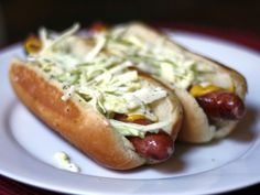 two hotdogs with coleslaw and mustard on a white plate