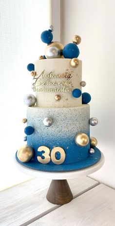 a three tiered blue and white cake with gold decorations on the top, sitting on a wooden stand