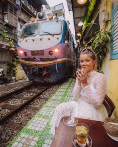 a woman sitting at a table in front of a train eating food and drinking tea