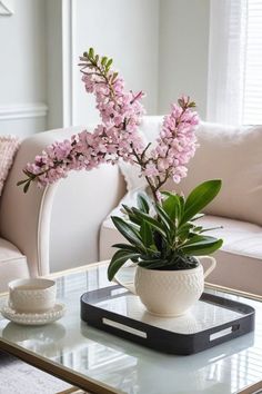 a living room with a couch, coffee table and pink flowers in a white vase