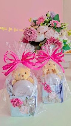 two teddy bears sitting in small baskets with pink ribbon and flowers on the table next to each other