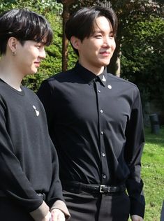 two young men standing next to each other in front of some trees and green grass