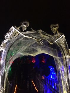 an archway decorated with halloween decorations and skeletons on it's sides, lit up at night