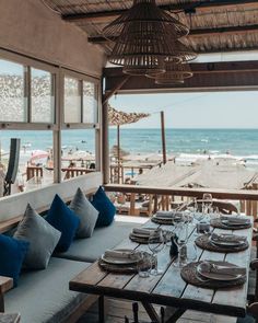 an outdoor dining area overlooking the ocean with blue cushions and place settings on wooden tables