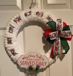 a white wreath with red and green bows hanging from it's side next to a door