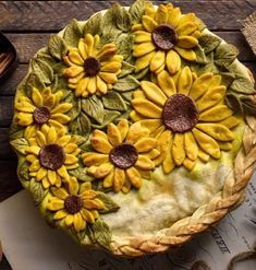 a pie with sunflowers on it sitting next to an apple and cinnamon sticks