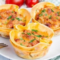 four mini lasagna cups on a plate with a fork and tomatoes in the background