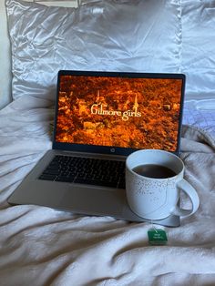 an open laptop computer sitting on top of a bed next to a cup of coffee