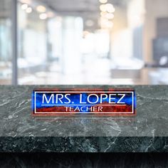 a blue and red teacher sign sitting on top of a marble counter in an office building