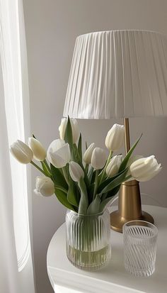 white tulips in a glass vase next to a lamp