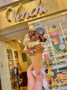 a person holding up an ice cream cone in front of a store with the words venchi on it