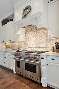 a kitchen with white cabinets and stainless steel stove top oven in front of a clock on the wall