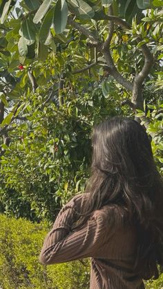 a woman standing in front of a tree with her back to the camera and looking at it