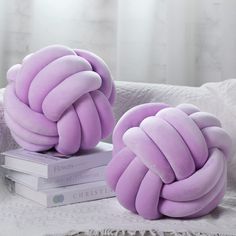 two purple pillows sitting on top of each other next to a stack of books in front of a window