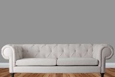 a white couch sitting on top of a hard wood floor next to a gray wall