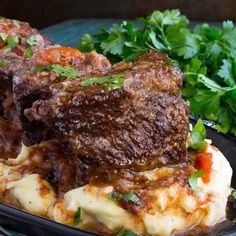 a black plate topped with meat covered in sauce and garnished with parsley