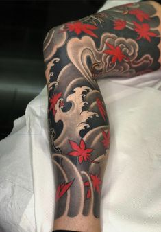 a man's arm covered in tattoos with red flowers and waves on the side