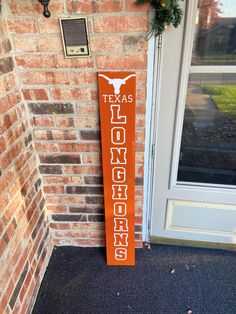 the texas longhorns wooden sign is next to a brick building with a wreath on it