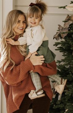 a woman holding a child near a christmas tree