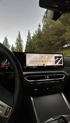 the dashboard of a car with an electronic device on it's display and trees in the background