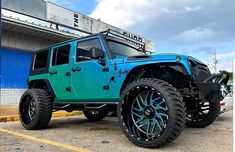 a blue jeep parked in front of a building with black rims and tires on it