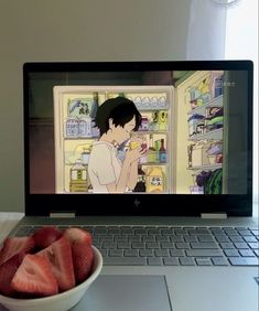 a bowl of strawberries sits in front of a laptop with the image of an anime on it