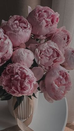 a bouquet of pink peonies in a vase on a table next to a mirror