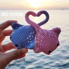 two small crocheted cats are being held in front of the ocean