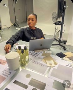 a woman sitting at a table working on a laptop computer surrounded by papers and other items