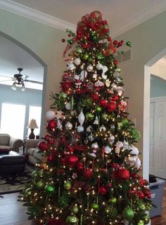 a decorated christmas tree in the middle of a living room with red and green ornaments