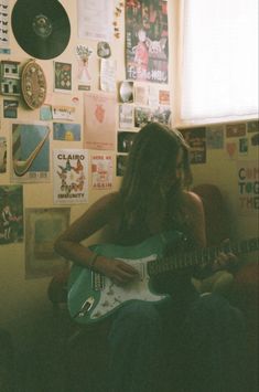 a person sitting in a room with a guitar and various pictures on the wall behind them