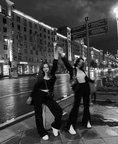 two women are dancing on the sidewalk in front of some tall buildings at night time