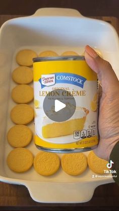 a person holding a can of lemon custard cookies in front of a white container