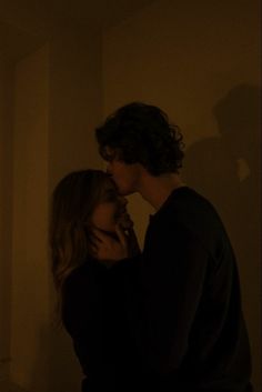 a man and woman standing in the dark with their faces touching each other's noses