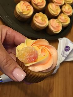 a hand holding a cupcake with frosting and candies on it next to other cupcakes