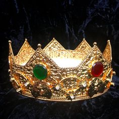 a gold crown with red, green and yellow stones on the front is sitting on a black velvet surface