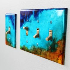 two light switch plates on a wall with blue and orange paint splattered on them