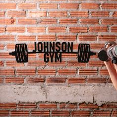 a person holding a pair of dumbbells in front of a brick wall with the words johnson gym written on it