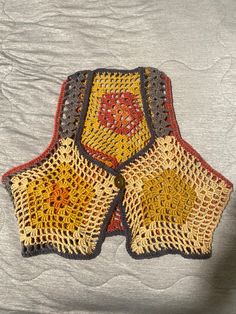 a crocheted dishcloth is laying on top of a white bed sheet with an orange and yellow design